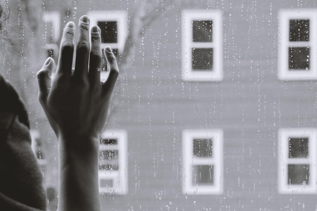 On the image there is a closeup of a person standing near a window. That person is holding it's hand against the window, like it is lonely. It is raining outside. This image demonstrates the presence of a narcissist in someone's life.