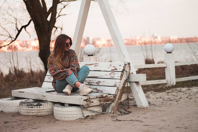 On the image there is a woman sitting on a bench. She is sitting near a lake. It looks like she is contemplating on her own personal growth plan.