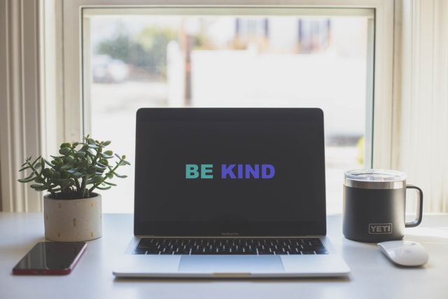 On the image, there is a computer with the words 'be kind' as a wallpaper.