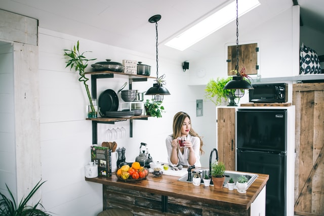 On the image, there is a woman sitting in the kitchen and drinking a cup of coffee.