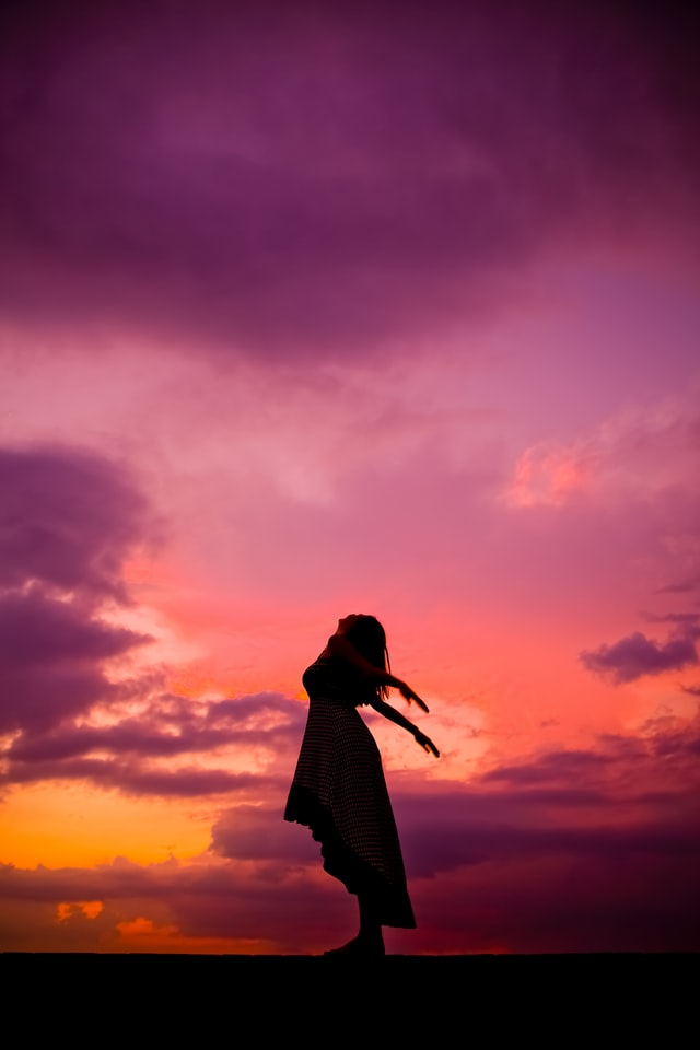 On the image, there is a woman standing on the beach and leaning towards the sky, with her arms spread out wide. It looks like she is taking in nature. Photo credits: Slava