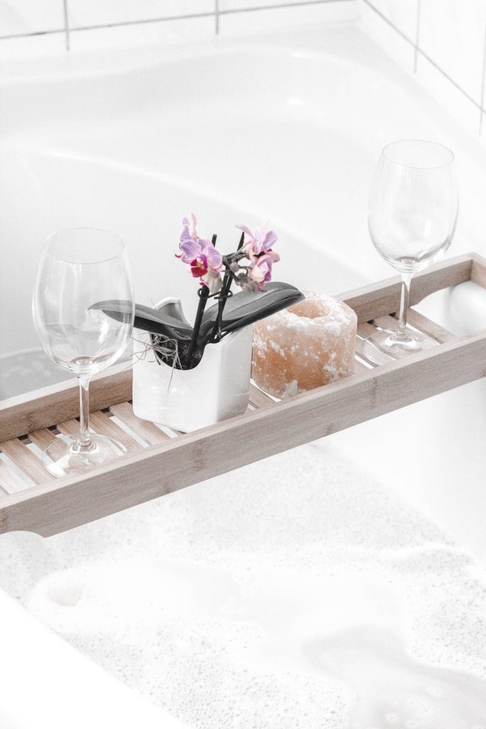 Bathtub tray with a small flowerpot, candle, and two wine glasses on it used by a Highly Sensitive Person taking a relaxing bath. Photo Credit: Mutzii