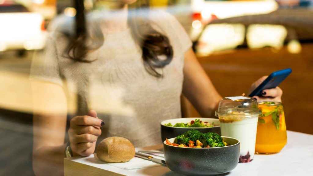 A highly sensitive woman sits at a table for lunch. In front of her are several healthy options for her to eat, such as vegetables, yogurt, and juice. Photo Credit: Farhad Ibrahimzade